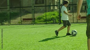 Group of boys playing football on sport playground in sunny day . Many kids play soccer in stadium with green grass and gate . Training , competition , healthy activity for children . Slow motion