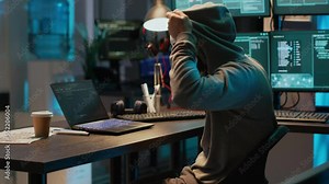Masked scammer hacking computer network late at night, working on laptop and multiple monitors to steal IT information. Hacker with hidden identity breaking security server, cyber attack.