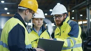 Three Industrial Engineers Talk with Factory Worker while Using Laptop. They Work at the Heavy Industry Manufacturing Facility.