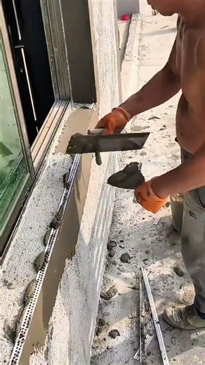 Worker applying cement plaster around window frame using trowel and straight edge