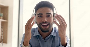 Happy charming young Arab blogger man in big wireless headphones talking on video call, speaking at online conference, enjoying communication, using Internet technology for broadcasting, streaming