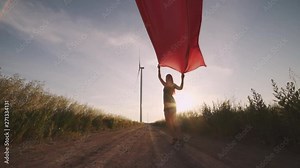 Woman with pieces of red cloth dance near the field with wind generators . Windmill on sunset. Slow motion. Stylish hipster woman