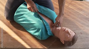 Close-up of middle-aged Asian male hands performing cardiopulmonary resuscitation (CPR) on a training dummy. Vital techniques include defibrillation, chest compressions, and maintaining the airway.