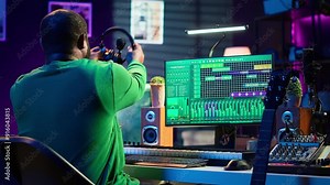 Producer composing new music on acoustic instrument in home studio, using microphone to sing chords. Musician songwriter works with mixing console and software, guitarist producing tunes. Camera A.