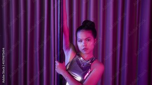 Portrait of confident female Asian pole dancer holding pole and looking at camera in studio
