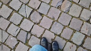Women's feet walk along the paving stones in the park, first-person view. Close-up of human feet walking down the street in cool weather. Walk in spring or autumn