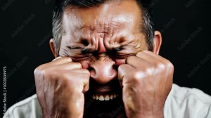 Stressed man clenching fists and squeezing eyes shut with intense expression on dark background, 4k video