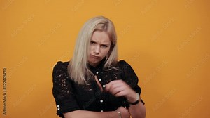 Beautiful blonde girl in black dress on yellow background an irritated woman shows negative attitude and an angry expression on face