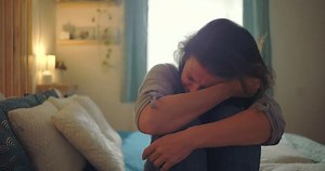 Woman sitting on bed, crying into her arm, overwhelmed by sadness and emotional pain, themes of grief, despair, and mental health struggles