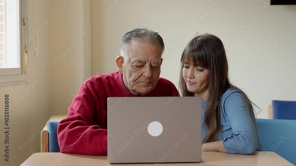Nurse patiently assists an elderly man in using a laptop, providing guidance and support in slow motion