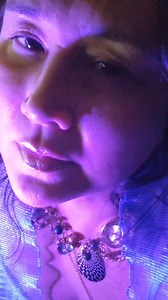 Music: "Teeth (interlude)" by xxxtentacion, instrumental version ~~~ #Accessibility #VideoDescription : Susan is wearing an iridescent aqua blue pleated organza scarf, a light blue camisole, frosted pink lip gloss, and a chunky upcycled charm necklace with a variety of trinkets and beads. She's lit with magenta light, the close-up of Susan's face and neck allowing for more detailed / emotive facial expression. With her head leaning back toward her left shoulder in contemplation, she pivots her h
