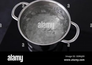 Stainless steel pot boiling water on black induction surface in modern kitchen interior. Steam, bubbles, and heat illustrate cooking process, sterilization, energy use, and domestic meal preparation Stock Video Footage - Alamy