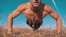 Young Athletic Man with a Bare Torso Performs Pushups on Nature. Slow...