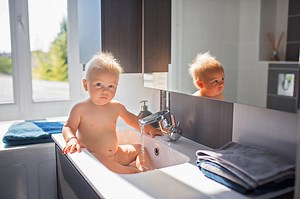 Baby taking bath in sink. Child playing with foam and soap bubbles in...