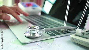 Doctor's writing and working on laptop computer, writing prescription clipboard with record information paper folders on desk in hospital or clinic, Healthcare and medical concept. Focus stethoscope