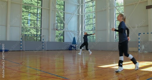 Girls practice the overhand serve. Female volleyball players take turns practicing serving the ball over the net.