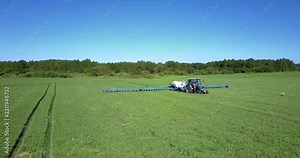tractor with trailer tank sprinkles soybean field with chemicals