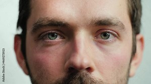Close up of Man's face. Attractive boy opening and closing his beautiful eyes. Caucasian young male model with blue, green, grey eyes looking at camera. Slow-motion, macro extreme close-up, 4K.