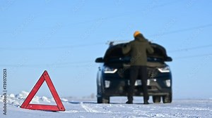 An emergency stop sign on the road and a man repairing a car in the background