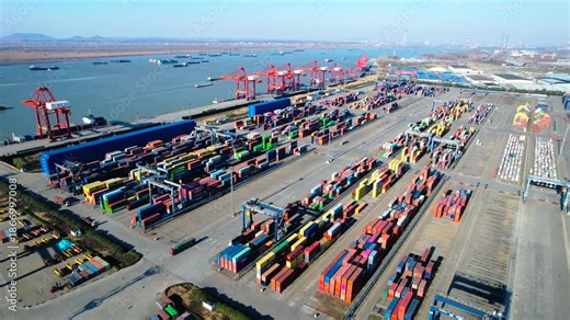 This dynamic industrial video captures the bustling operations of a busy logistics port and shipping terminal, showcasing massive container ships docking to load and unload cargo, towering port cranes