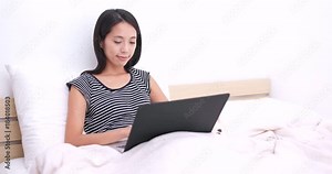 Woman working on laptop computer with her dog and sitting on bed
