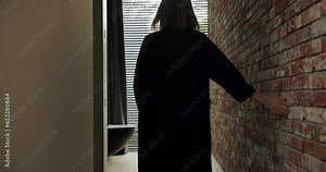 Woman go barefoot in hallway with loft interior and touch brick wall enjoying her house. Modern design and decoration at vacation home with glass wall