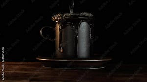 Cup overflows onto the saucer and table. Slow motion. Dark setting with natural light.