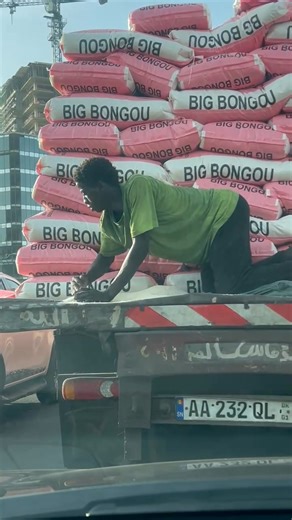 Ce jeune Sénégalais est en train de ramasser les grains de riz qui se sont échappés des sacs. Il répète ce geste plusieurs fois par jour, certainement pour avoir un stock à vendre pour quelques francs CFA ou en amener en guise de ravitaillement chez lui. Ce véhicule sortait du port Autonome de Dakar. | Seydina Omar Ba