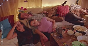 Friends passed out on couch and floor after party. Empty plates and glasses on table. Aftermath of a wild night.