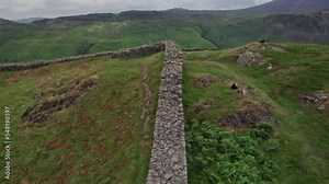 Slow low aerial over remains of Hardknott Roman Fort rampart in green hilly landscape, Eskdale valley, Lake District, Cumbria, UK