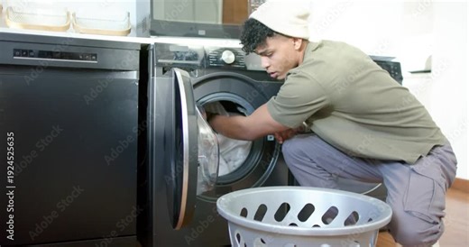 Man is crouching, reaching into front-load washer loading white clothes closing door starting wash