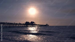 Sunset over sea with small boat. Sunset of sun setting over ocean. Tranquil idyllic scene of a sunset over sea with reflection. Reflected sun on a water surface. People walking on pier at sunset time.