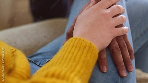 Close shot of two hand who touch and caress each other on the legs of one of them One hand is white and one is brownish Trousers are blue jeans and she wears a sweater Symbolic and profound gesture