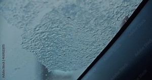 Cleaning a car windshield with an ice scraper, freezing rain over night covered the hole windshield. Dark and moody shot.