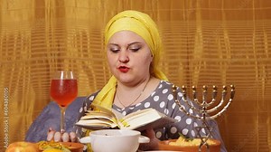 A Jewish woman at a set table for Shabbat makes kiddush for wine. Overall plan.