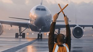 Airport Ground Crew Member Marshalling Commercial Aircraft On Wet Tarmac During Sunrise