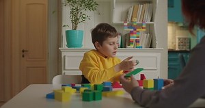 Autistic boy building with color wooden blocks. Teacher gives assignment to pupil with autism. Applied behavior analysis therapist working with kid.