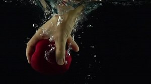 Man hand reaches and grabs red apple floating under water super slow motion shot