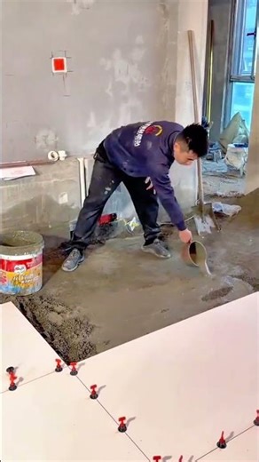 Worker pouring mortar while installing ceramic floor tiles indoors