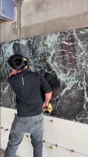 the process of installing large patterned black ceramic tiles on the walls in a room in a building