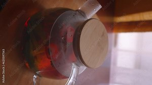Process of brewing tea, tea ceremony, freshly brewed fruit and herbal tea. Spoonful stirs tea in teapot with tea leaves, mint, strawberries and fruit in glass teapot on table. close-up.