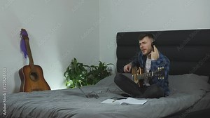 Man emotionally singing and playing on electric guitar at home. Young caucasian male in headphones and blue t-shirt plays on guitar. Musician practicing new lyric song. Music concept. Slow motion
