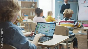 Elementary School Science Class: Over the Shoulder Little Boy Uses Laptop with Screen Showing Programming Software. Physics Teacher Explains Lesson to a Diverse Class full of Smart Kids