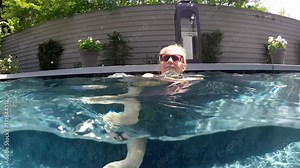Camera half above and half below water, a beautiful, slim, caucasian woman wearing string bikini swims from left to right. Camera follows her.
