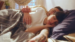 Young affectionate man caressing hand of sleeping girlfriend when taking a nap together during the day at home