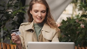 Attractive student girl sitting in street cafe with credit card checking her bank account on laptop using free internet connection. Modern technology