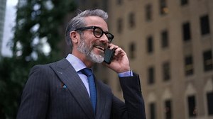 Successful man in expensive suit talks on mobile phone device in the city. Busy entrepreneur on phone call discussing important business issues while standing outdoors in downtown