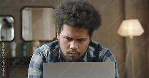 Young black man working on laptop. Man engrossed in work in front of laptop. Black young man working hard and enthusiastically on laptop. African-American guy solves business problems, working hard.