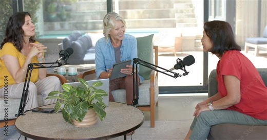 Diverse female hosts reading tablet as guest entering from left, joining podcast with mics at home