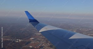 Airplane wing view out window with fluffy clouds in sky backed by background of earth